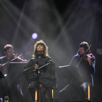 Koncert Natalii Kukulskiej, za nią siedzący mężczyźni grający na skrzypcach