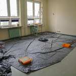Sala lekcyjna podczas remontu, na podłodze leży folia, na której znajdują się farby oraz drabina