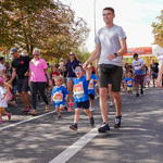 Chłopiec w okularach trzyma za rękę ojca podczas biegu, w tle: uczestnicy biegu