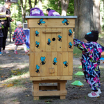 Dziecko stoi obok drewnianego ulu, na którym namalowane są niebieskie pszczółki