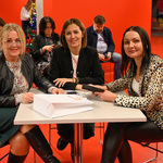 Trzy uśmiechnięte kobiety siedzą przy stole 