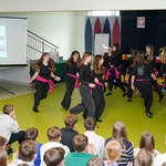 Uczestnicy spotkania podczas tańca w czarnych strojach oraz różowych opaskach owiniętych wokół bioder, w tle: publiczność 