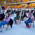 Mieszkańcy siedzący na płycie stadionu na rozkładanych krzesłach z zachowaniem odległości