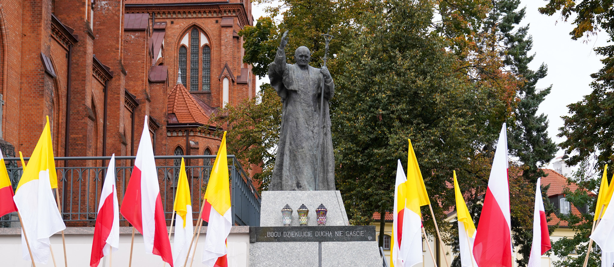Pomnik Jana Pawła II udekorowany flagami w barwach narodowych, a także miasta Białystok oraz złożone kwiaty