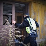 Strażnik miejski zagląda do drewnianego, opuszczonego domu