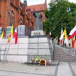 Pomnik Jana Pawła II, pod którym leżą kwiaty i stoją znicze
