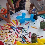 Zbliżenie na stół artystyczny, na którym dzieci malują drewniane zawieszki w kształcie drzew, kolorują mazakami
