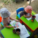 Dzieci siedzące przy plastikowych stolikach, kolorujące kredkami obrazki