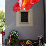 Tablica upamiętniająca Icchocka Malmeda i leżące pod nią wieńce, w pierwszym planie u góry kadru powiewające flagi Polski i Białegostoku