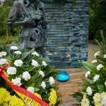 Pomnik Inki otoczony kwiatami, przed nim pali się stojący na ziemi duży niebieski znicz