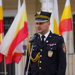 Komendant Straży Miejskiej przemawia do mikrofonu, za nim powiewają flagi w barwach Białegostoku