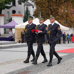 Trzech Strażników Miejskich uroczyście niosących flagę Polski przez plac