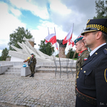 Po prawej mundurowi stojący na baczność, w oddali widać pomnik i stojących na warcie żołnierzy