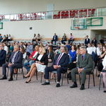 Goście honorowi uroczystości siedzący na krzesełkach w dużej sali gimnastycznej