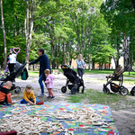 Wykładzina z klockami rozłożona w parku, wokół rozstawione wózki spacerowe, rodzice obserwujący dzieci