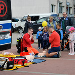 Ratownik medyczny instruujący mężczyznę jak przeprowadzić pierwszą pomoc, obok stojące dzieci obserwują sytuację