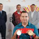 Rafał Czuper trzymający medale, w tle rozmazane postacie trzech osób