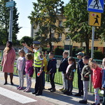 Dzieci wraz z funkcjonariuszkami Straży Miejskiej stoją przed przejściem dla pieszych