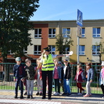Dzieci wraz z funkcjonariuszkami Straży Miejskiej stoją przed przejściem dla pieszych
