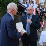 Mężczyzna trzyma medal w dłoniach, drugi przemawia do mikrofonu