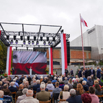 Szeroki kadr podczas przemówienia Andrzeja Dudy, który stoi na scenie na tle telebimu i wyświetlanej na nim flagi Polski