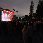 Po lewej stronie rozświetlona scena, po prawej publiczność słuchająca koncertu