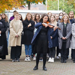 Uczennica grająca na skrzypcach, za nią stojąca młodzież i nauczycielka