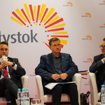 Trzech mężczyzn siedzących w fotelach podczas konferencji, pierwszy z lewej strony Przemysław Tuchliński przemawia do mikrofonu