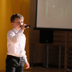 Chłopiec w białej koszuli śpiewa do mikrofonu