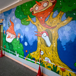 Mural na ścianie korytarza wewnątrz budynku szkoły przedstawiający np. dzięcioła wychylającego się z dziupli w drzewie, krasnala wyskakującego z krzaków