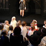 Młoda kobieta śpiewająca ze sceny, na widowni małe dzieci