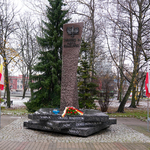 Pomnik Armii Krajowej na tle parku i złożony pod nim wieniec oraz zapalony znicz