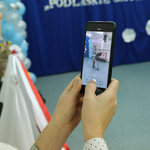Kadr z telefonem, na którym kobieta nagrywa występ dzieci podczas uroczystości