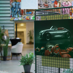 Po prawej wizualizacja sportowego kabrioletu na tablicy wiszącej na kratowanej ściance, w tle widać halę oraz stoiska wystawowe