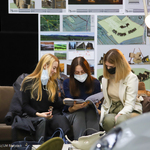 Trzy dziewczyny siedzące na kanapie, oglądają magazyn, za nimi na tablicy projekt architektoniczny budynku