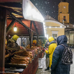 Ludzie kupujący swojskie kiełbasy przy stoisku na jarmarku świątecznym późnym wieczorem, z nieba pada puszysty śnieg