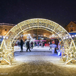 Instalacja świetlna na zaśnieżonym Rynku Kościuszki w kształcie łuku, w tle spacerujący po jarmarku ludzie