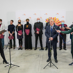 Prezydent Tadeusz Truskolaski wypowiada się do mikrofonu, za nim stoją w rzędzie nagrodzeni artyści