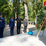 Dyrektor Departamentu Prezydenta Miasta Jacek Brzozowski stawia znicz przy pomniku na cmentarzu wojskowym. Asystują przedstawiciele służb mundurowych