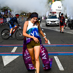 Kobieta przekraczająca metę ma na sobie zerwaną szarfę, w tle prezentowany czas biegu, mężczyzna na rowerze oraz biegnący w stronę mety uczestnicy