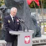 Tadeusz Chwiedź- prezes zarządu głównego Związku Sybiraków przemawia z mównicy, w tle pomnik upamiętniający Bohaterskie Matki Sybiraczki, przy którym stoi warta