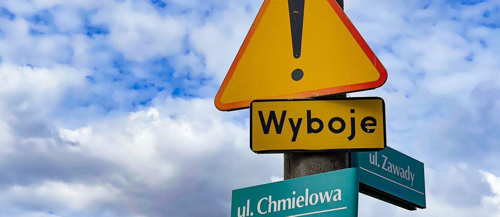 Słup ze znakami drogowymi informującymi o wybojach oraz z nazwami ulic: Chmielowa i Zawady