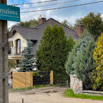 Słup z tablicą informującą o nazwie ulicy (Szyszkowa), widok na drogę szutrową i domy