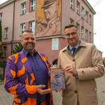 Jeden z twórców muralu Dariusz Paczkowski i zastępca prezydenta Rafał Rudnicki pozują do wspólnego zdjęcia z projektem muralu, za nimi widać w całej okazałości mural