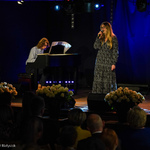 Kobieta w długiej sukience śpiewa na scenie, w tle: mężczyzna gra na pianinie