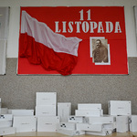 Biało-czerwona flaga Rzeczypospolitej Polskiej. Obok napis 11 Listopada oraz portret Marszałka Józefa Piłsudskiego