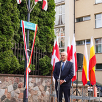 Prezydent Tadeusz Truskolaski zabiera głos podczas wydarzenia, obok wisi tablica Skwer Wolnej Białorusi