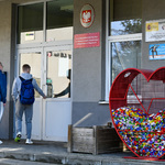 Uczniowie wchodzą do budynku szkoły, obok którego stoi serce z nakrętkami