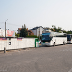 Dwa autobusy stoją na parkingu, obok znajduje się paczkomat oraz bankomat