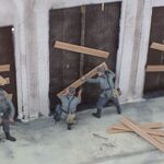 Fragment dioram K. Chojnackiego, mężczyźni przybijają deski do drzwi